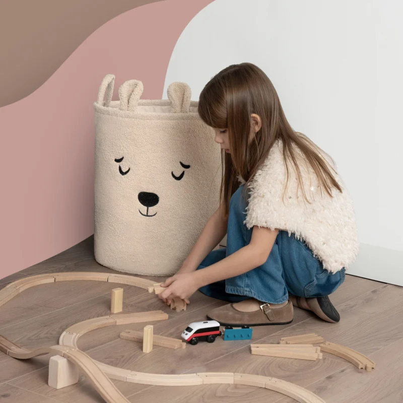 SIPO beżowy kosz na zabawki premium bouclé w kształcie misia obok dziecka układającego tory.