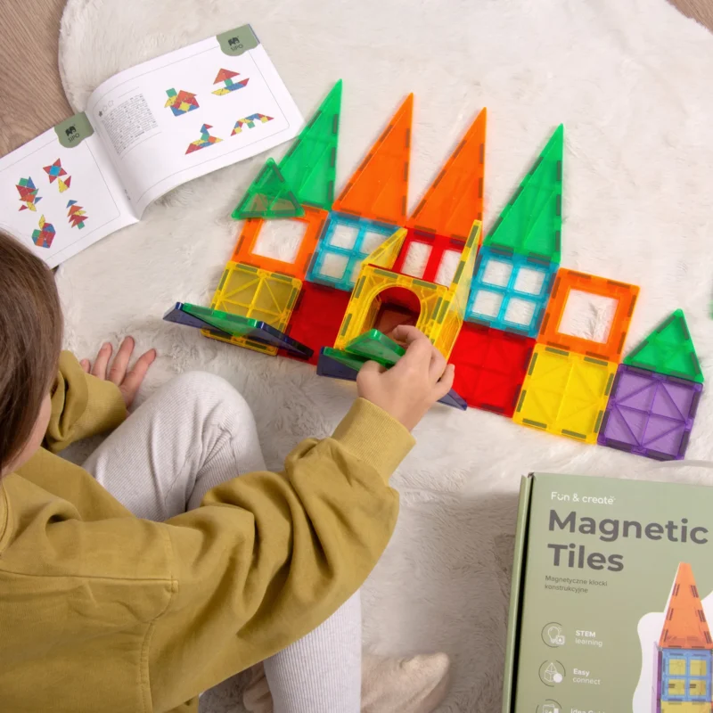 Dziecko układa zamek z klocków SIPO Magic Castles na dywanie, obok przewodnika budowania.